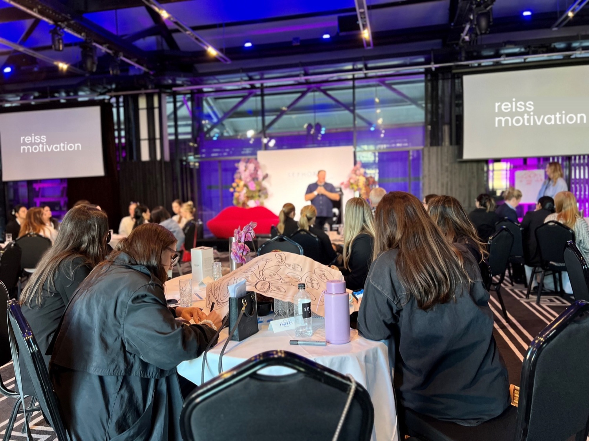 Sephora leaders in a Reiss Motivation session, seated at round tables facing the stage.